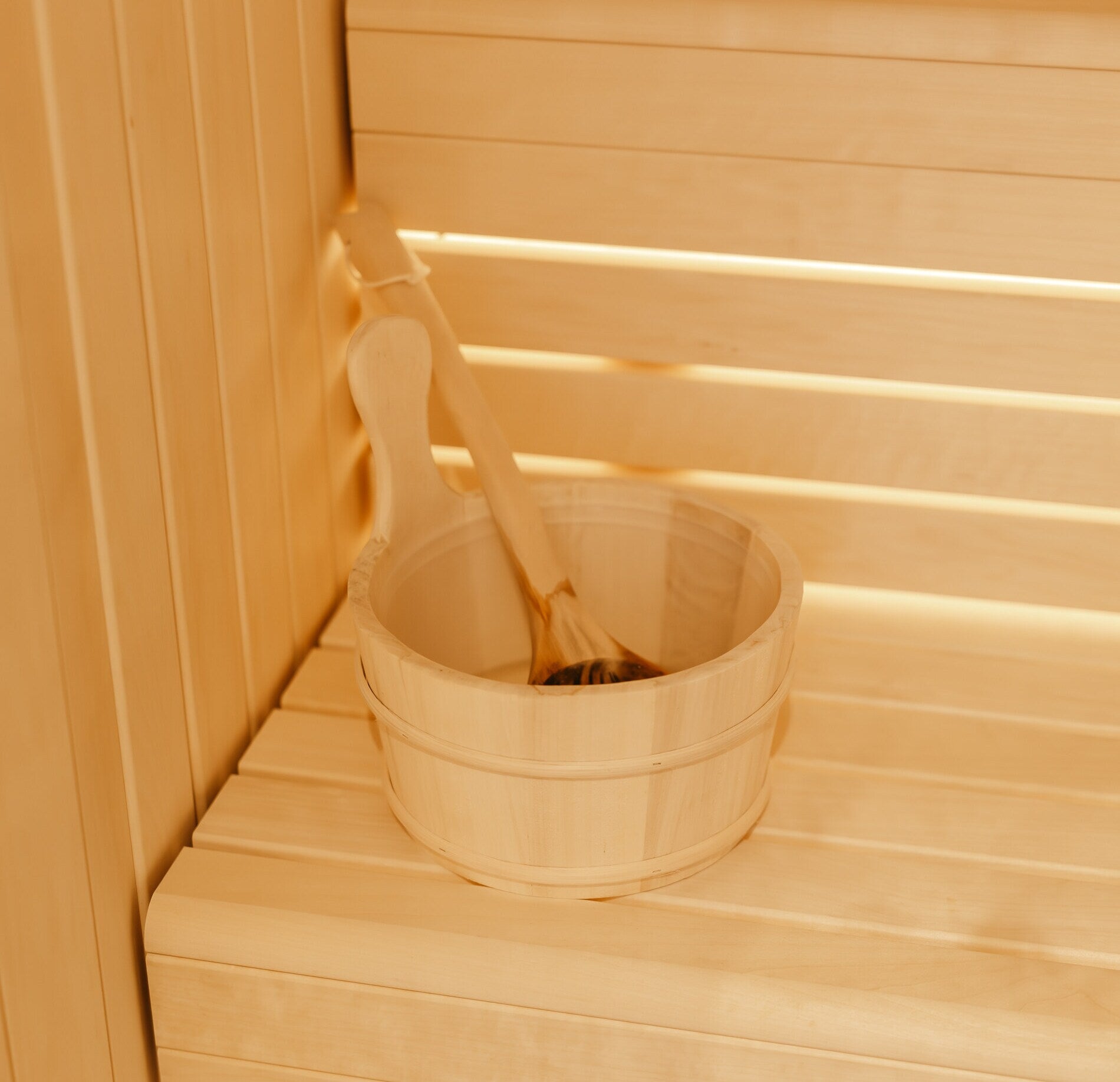 Un seau en bois avec une louche repose sur un banc dans un sauna lumineux du spa de la maison le Goyen, entouré de parois en bois clair.
La lumière chaude souligne les textures lisses du bois et crée une ambiance intime et apaisante propice à la détente.