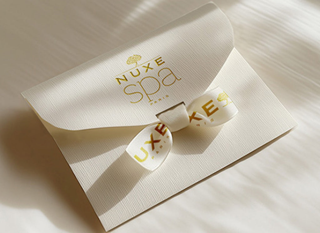 Carte cadeau NUXE Spa présentée dans une élégante pochette blanche avec ruban personnalisé, symbole d’une expérience bien-être et de soins premium.