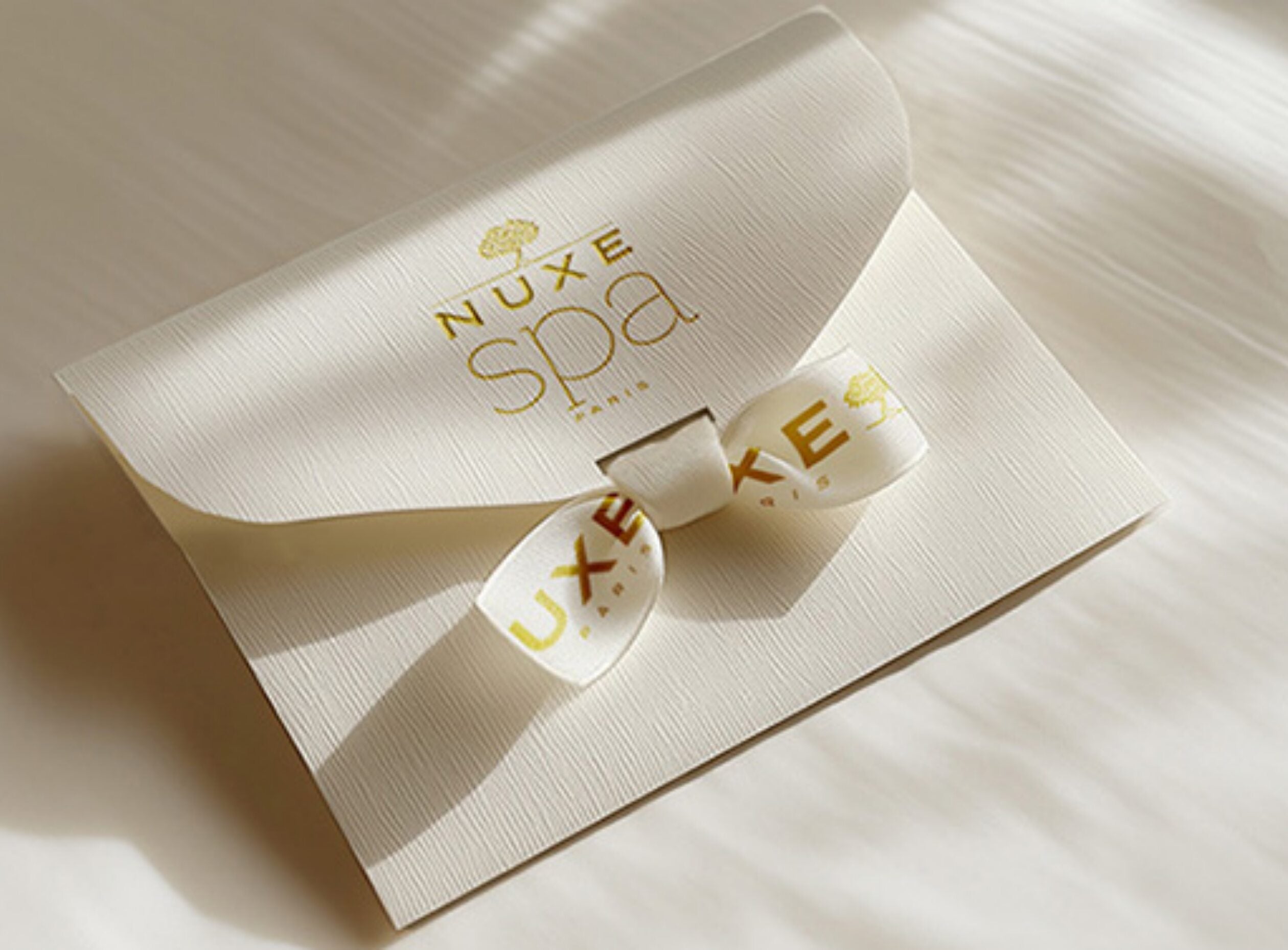 Carte cadeau NUXE Spa présentée dans une élégante pochette écrue fermée par un ruban personnalisé, idéale pour offrir une expérience de bien-être et de soins en spa.
