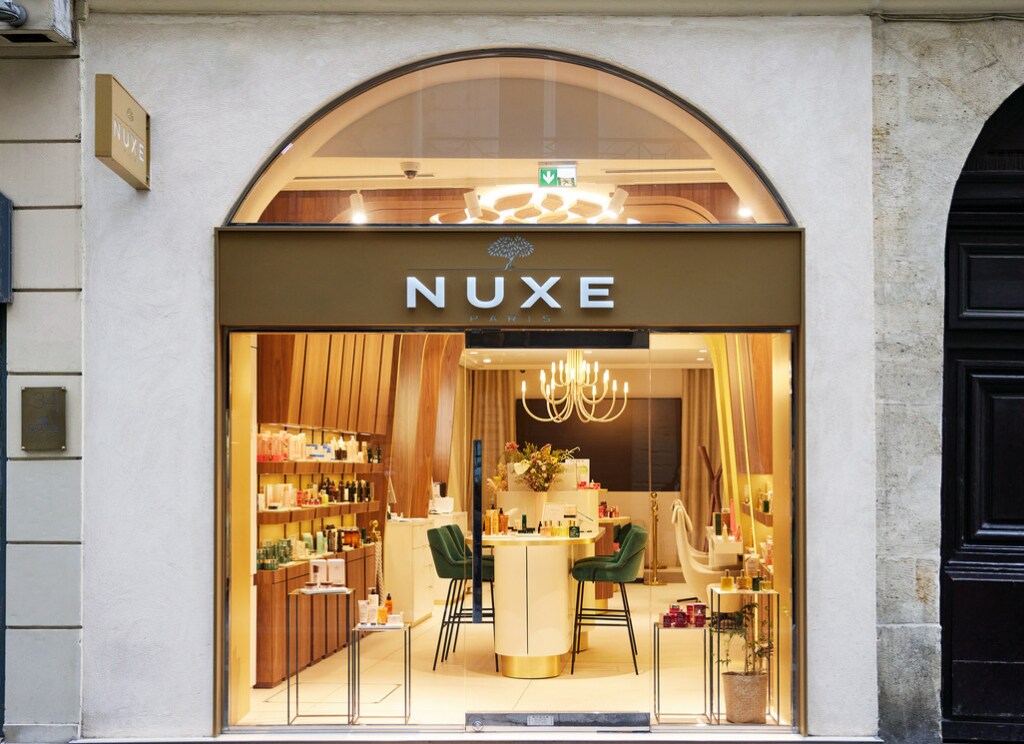 Boutique NUXE Paris avec large vitrine éclairée, présentation de produits de soin et de beauté dans un intérieur élégant aux finitions en bois