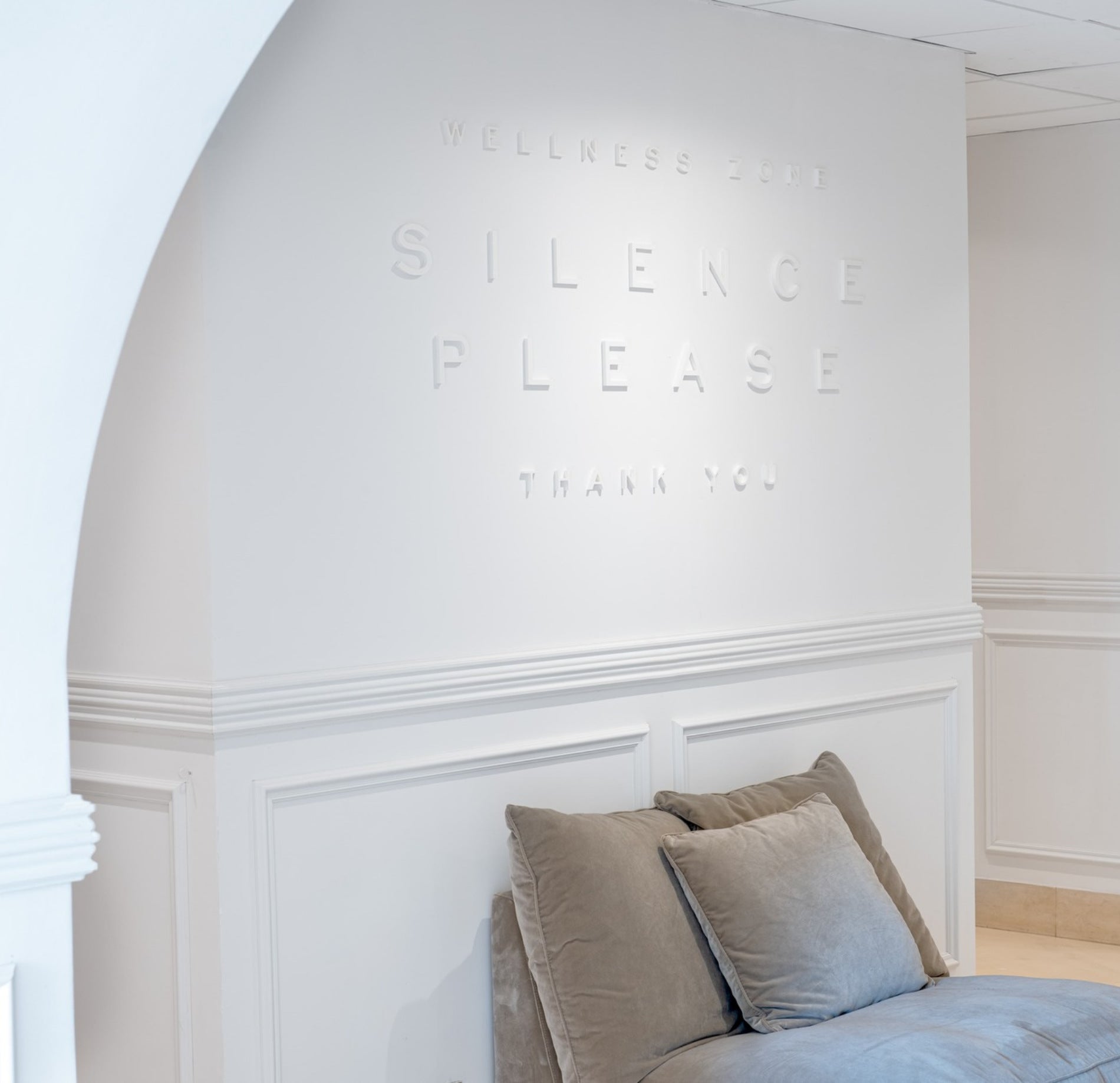 Espace de repos élégant et épuré du spa NUXE, aux murs blancs raffinés avec inscription discrète “Silence Please”, agrémenté d’un fauteuil confortable et d’une ambiance lumineuse apaisante invitant au calme et à la détente. 