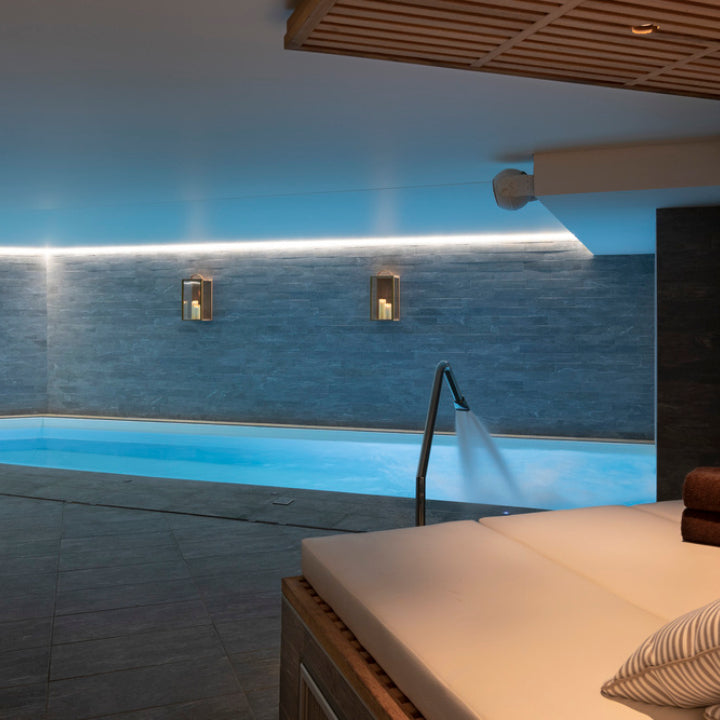 Un espace détente élégant du St'Alban Hotel & Spa, avec une piscine aux eaux bleu clair bordée de murs en pierre et soulignée par un éclairage diffus continu.
Au premier plan, un lit de repos rembourré complètent cette atmosphère calme, entre design contemporain et bien‑être.