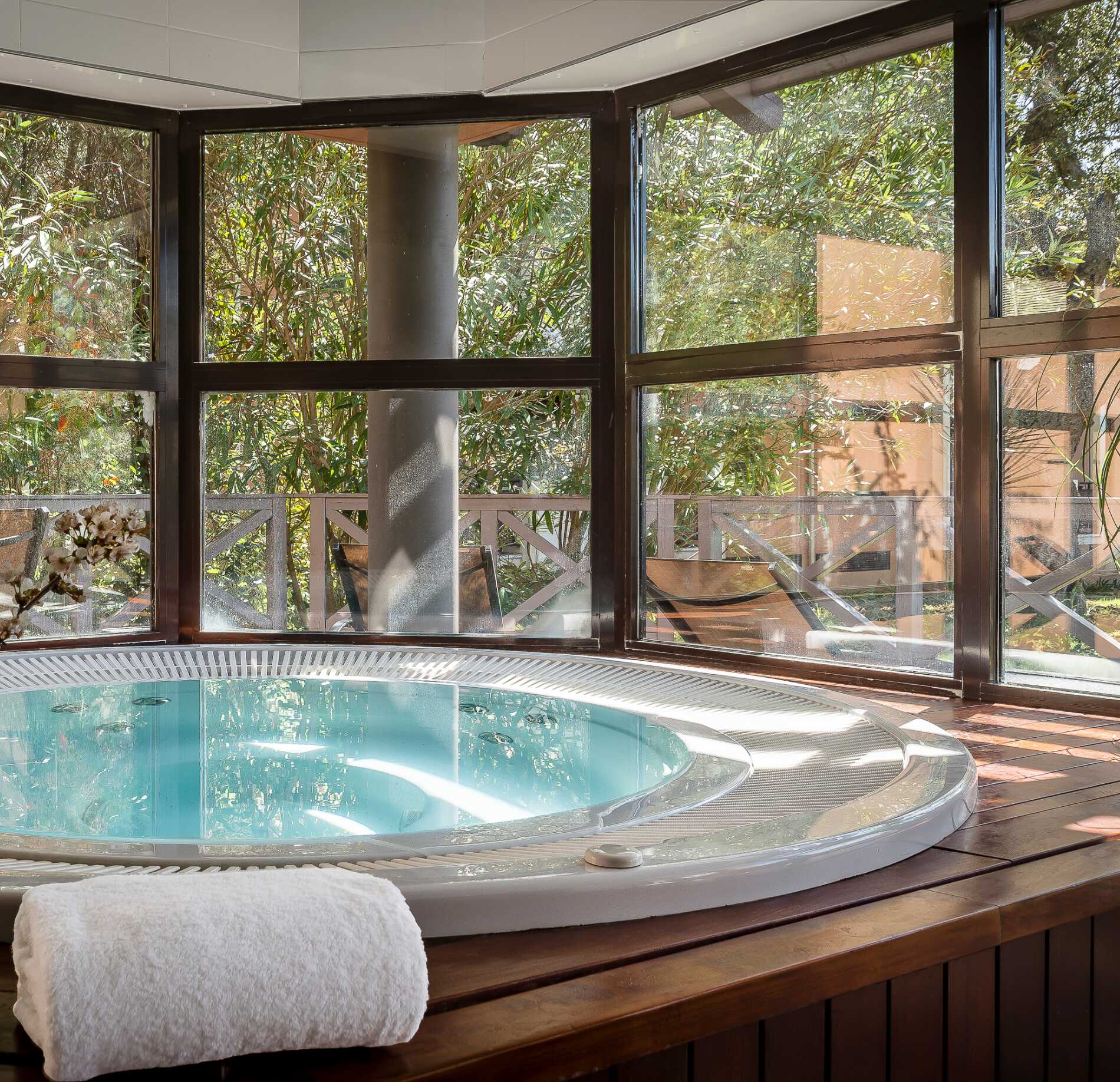 Jacuzzi lumineux du spa NUXE à l’Hôtel Valescure, encastré dans un habillage en bois chaleureux, entouré de larges baies vitrées offrant une vue apaisante sur une végétation verdoyante, dans une atmosphère naturelle, sereine et raffinée.