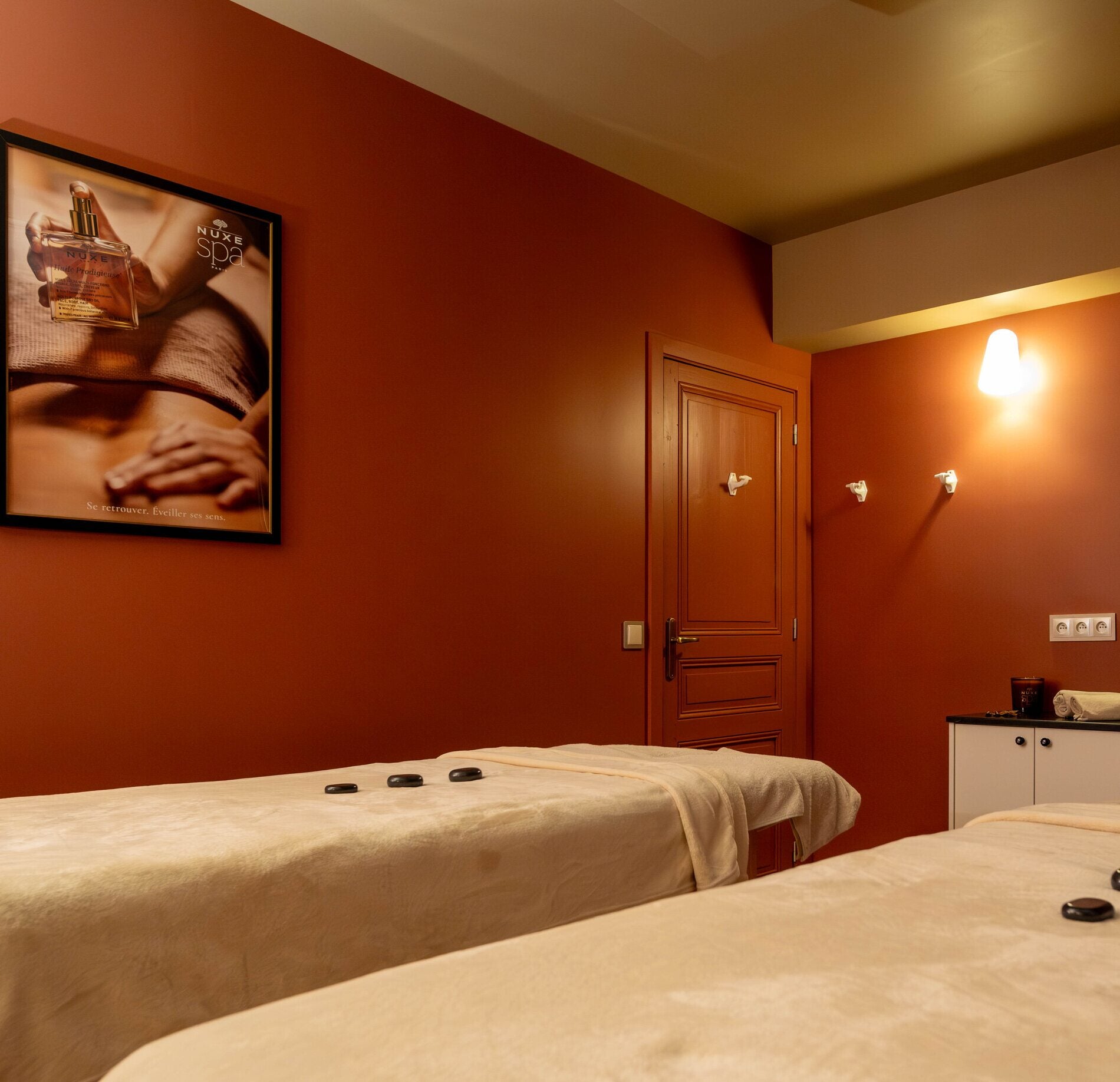 Cabine de soin élégante du spa NUXE, aux murs aux teintes chaleureuses, avec tables de massage confortables, éclairage doux et ambiance apaisante propice à une détente profonde.