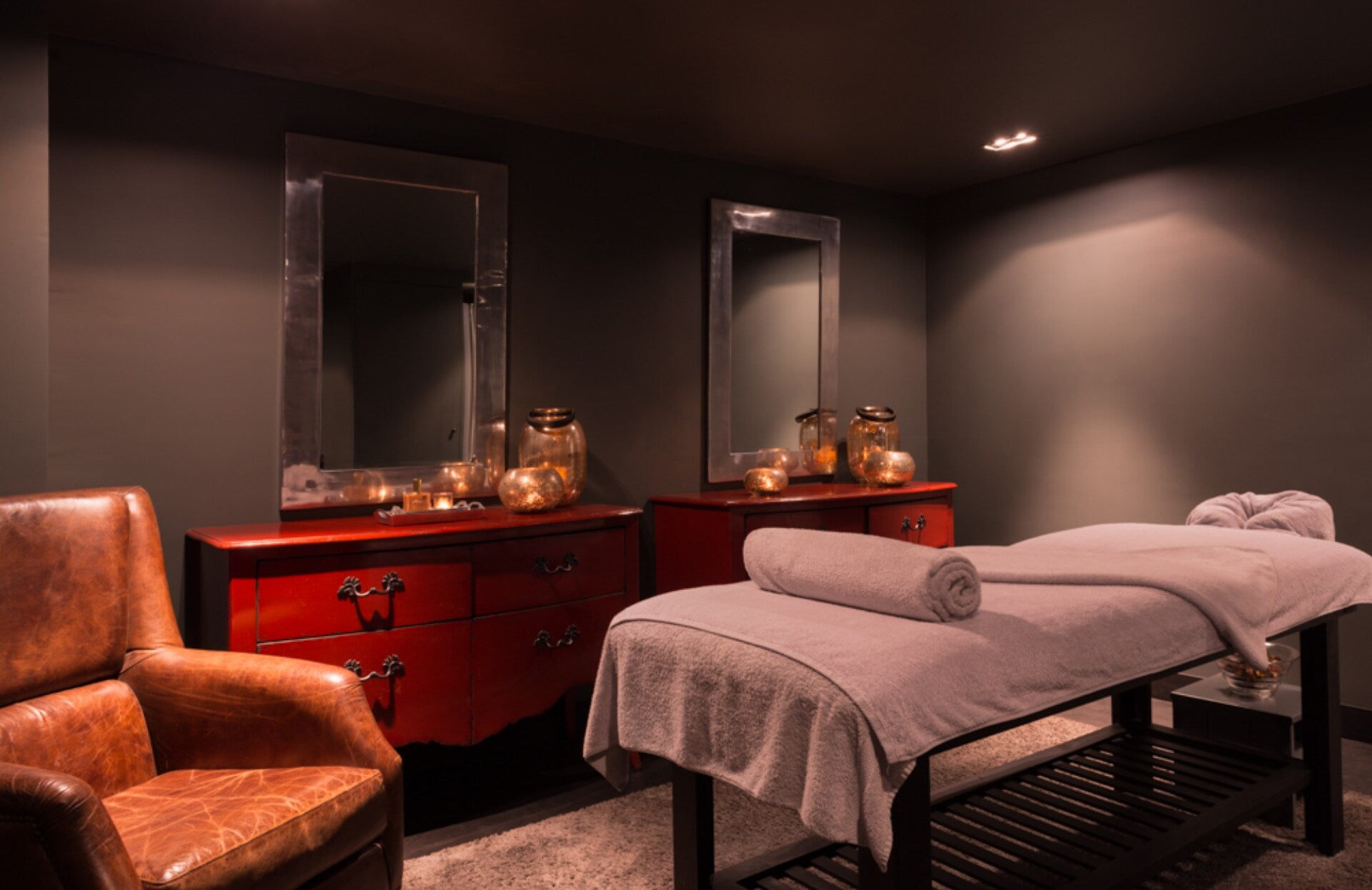 Une cabine de soin élégante et feutrée, où des tons chauds et des matières nobles créent une atmosphère intime et apaisante. Entre table de massage soigneusement préparée, lumière tamisée et mobilier raffiné, cet espace invite à un moment de détente absolue et de lâcher‑prise total.