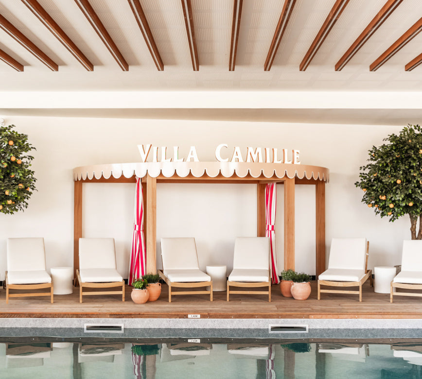 Un espace détente élégant du Spa la Villa Camille, avec des transats clairs parfaitement alignés face à une piscine aux reflets apaisants.
En arrière-plan, une structure en bois avec l’inscription “VILLA CAMILLE” et des rideaux rayés apporte une touche chaleureuse et raffinée, entourée de plantes verdoyantes.