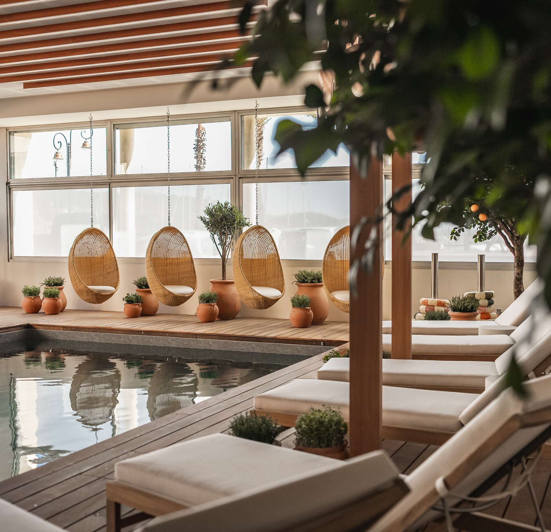 Un espace détente apaisant du Spa la Villa Camille, avec des fauteuils suspendus en rotin alignés face à une piscine aux reflets calmes.
Autour, des plantes en pot, une structure en bois et de larges fenêtres laissent entrer une lumière douce, créant une atmosphère naturelle et harmonieuse.
