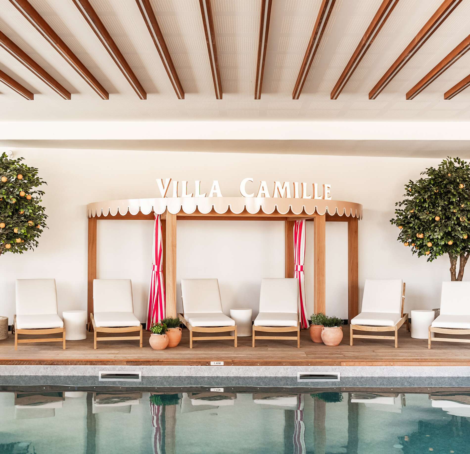 Un espace détente élégant du Spa la Villa Camille, avec des transats clairs soigneusement alignés face à une piscine aux reflets doux.
En arrière-plan, une structure en bois avec l’inscription “VILLA CAMILLE” et des rideaux rayés apporte une touche chaleureuse et sophistiquée, entourée de plantes verdoyantes.