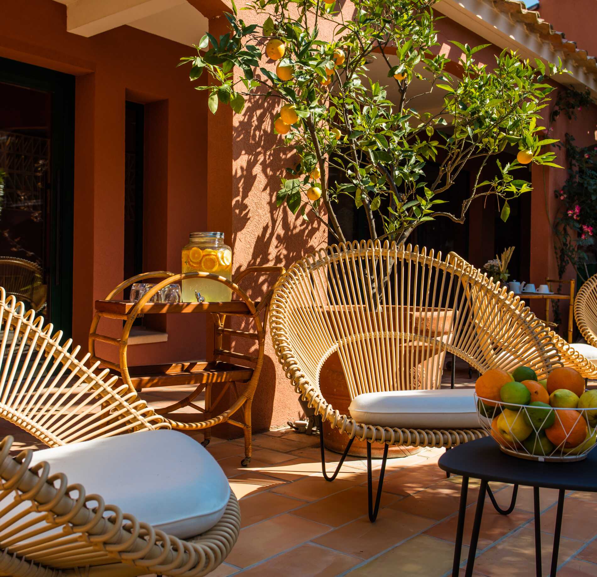 Un espace extérieur ensoleillé du Spa Villa Duflot, avec des fauteuils en rotin aux formes arrondies disposés autour de tables basses.
Un oranger chargé de fruits et des éléments en bois clair créent une ambiance chaleureuse et méditerranéenne, propice à la détente.