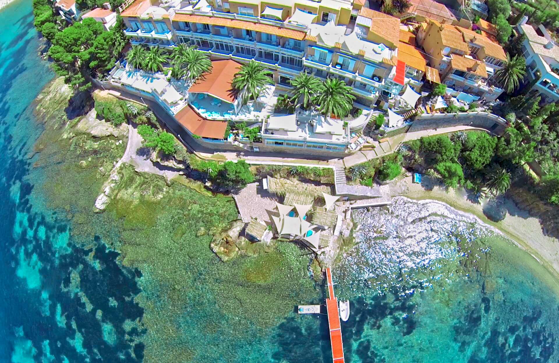 Une vue aérienne spectaculaire révèle l'établissement Vistabella niché en bord de mer, entouré de palmiers dominant une eau turquoise cristalline.
Un ponton s’avance vers la mer translucide et des espaces aménagés sur le rivage invitent à une expérience exclusive, alliant luxe, nature et évasion totale.