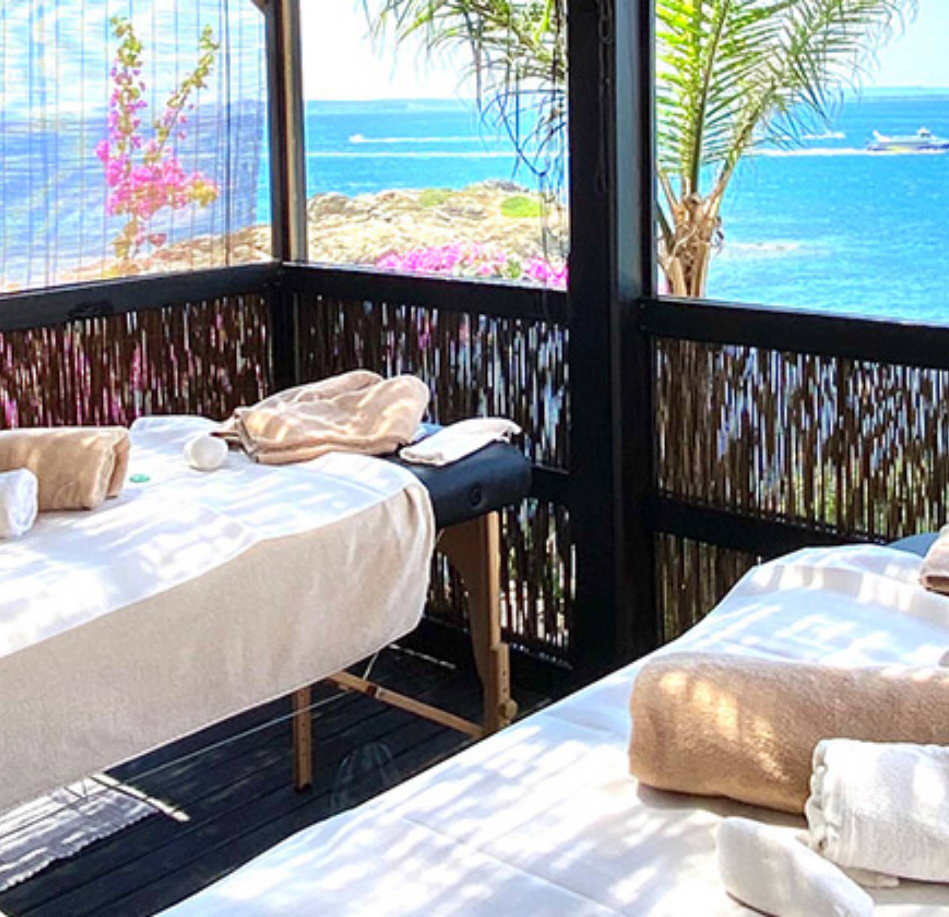 Une cabine de soin ouverte sur l’extérieur du Spa Hotel Vistabella, avec deux tables de massage recouvertes de linge clair et disposées face à la mer.
La structure en bois ajouré laisse apparaître une végétation colorée et une eau bleu éclatant, créant une ambiance lumineuse et apaisante propice à la détente.