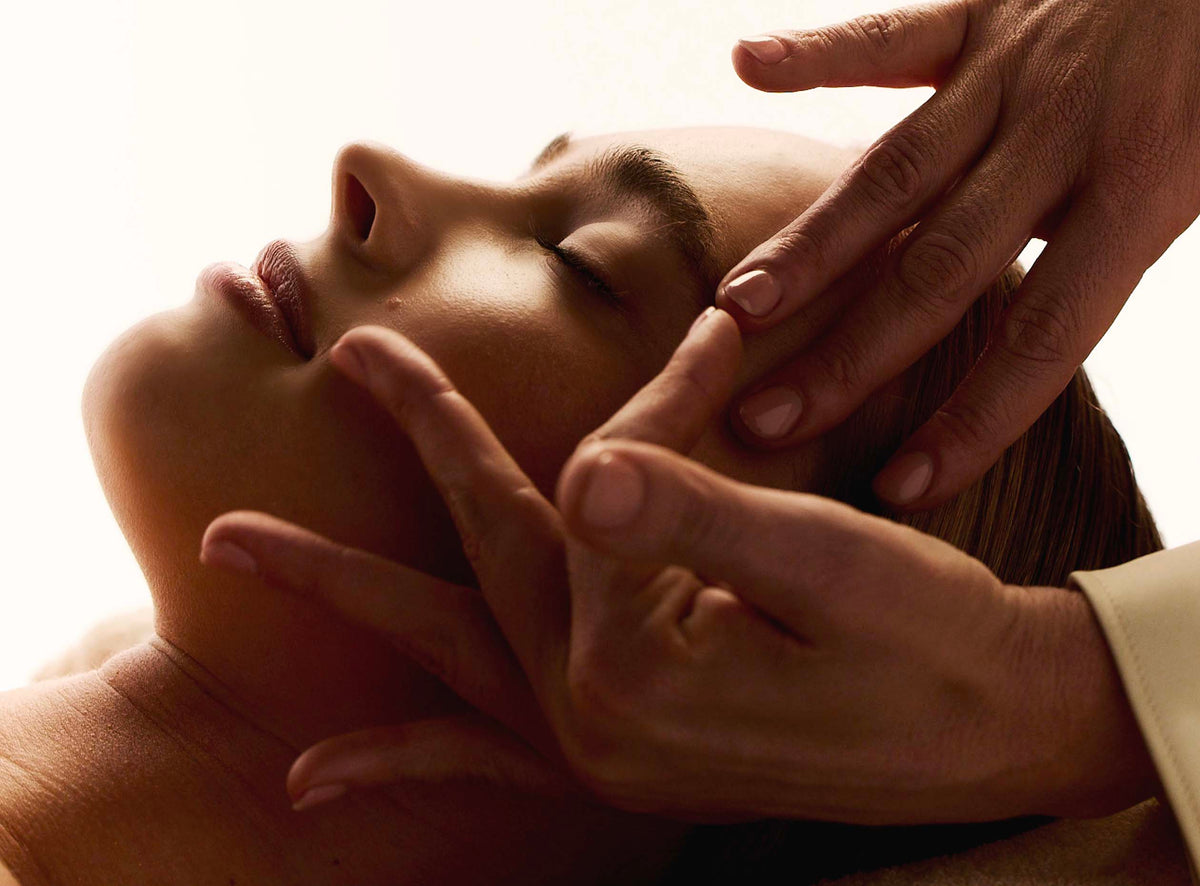 Femme allongée les yeux fermés pendant qu'une main fait glisser un outil de massage doré sous son œil