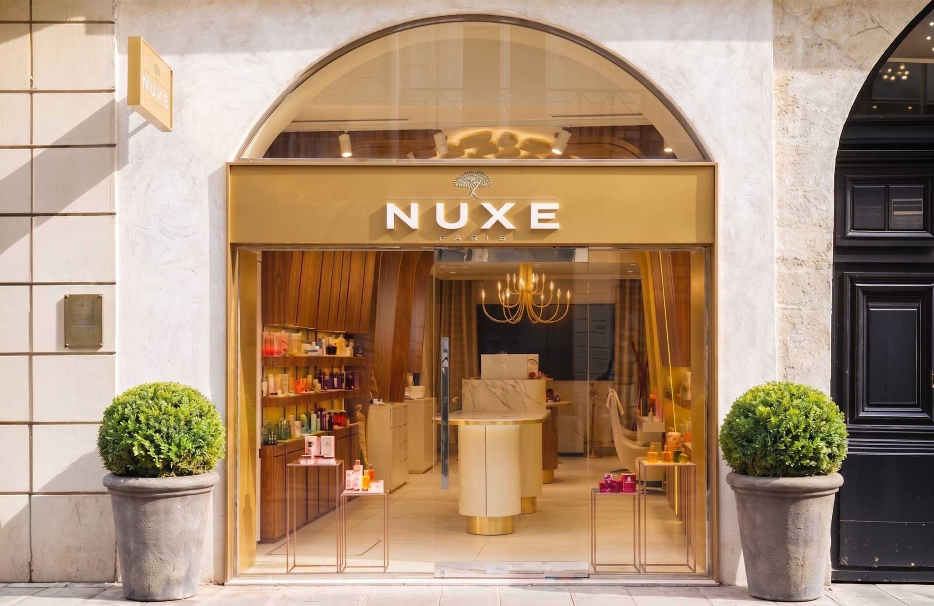Façade du Spa NUXE Montorgueil à Paris : vitrine en arche avec enseigne dorée, boutique de soins et lustre visibles à travers la porte vitrée